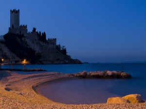 castello malcesine e spiaggia illuminata da luci lungolago